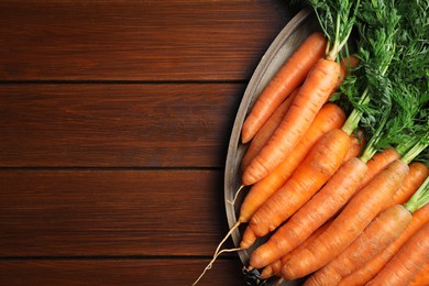 Many tasty fresh carrots on wooden table, top view. Space for text