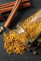 Photo of Jar with dry curry powder and other spices on dark textured table, flat lay