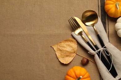 Photo of Cutlery, napkin and pumpkins on brown tablecloth, flat lay with space for text. Table setting