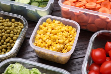 Plastic and glass containers with different fresh products on wooden table, closeup