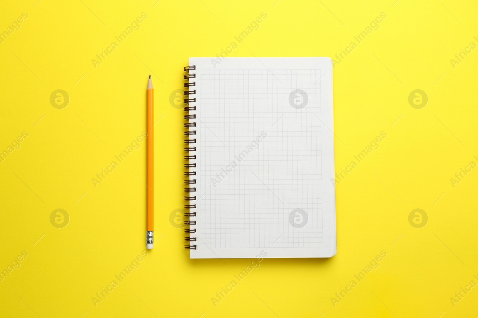 Photo of Notebook and pencil on yellow background, top view