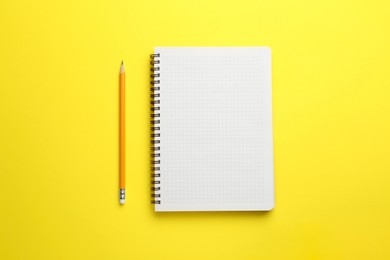 Photo of Notebook and pencil on yellow background, top view