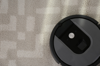 Photo of Modern robotic vacuum cleaner on carpet, top view. Space for text