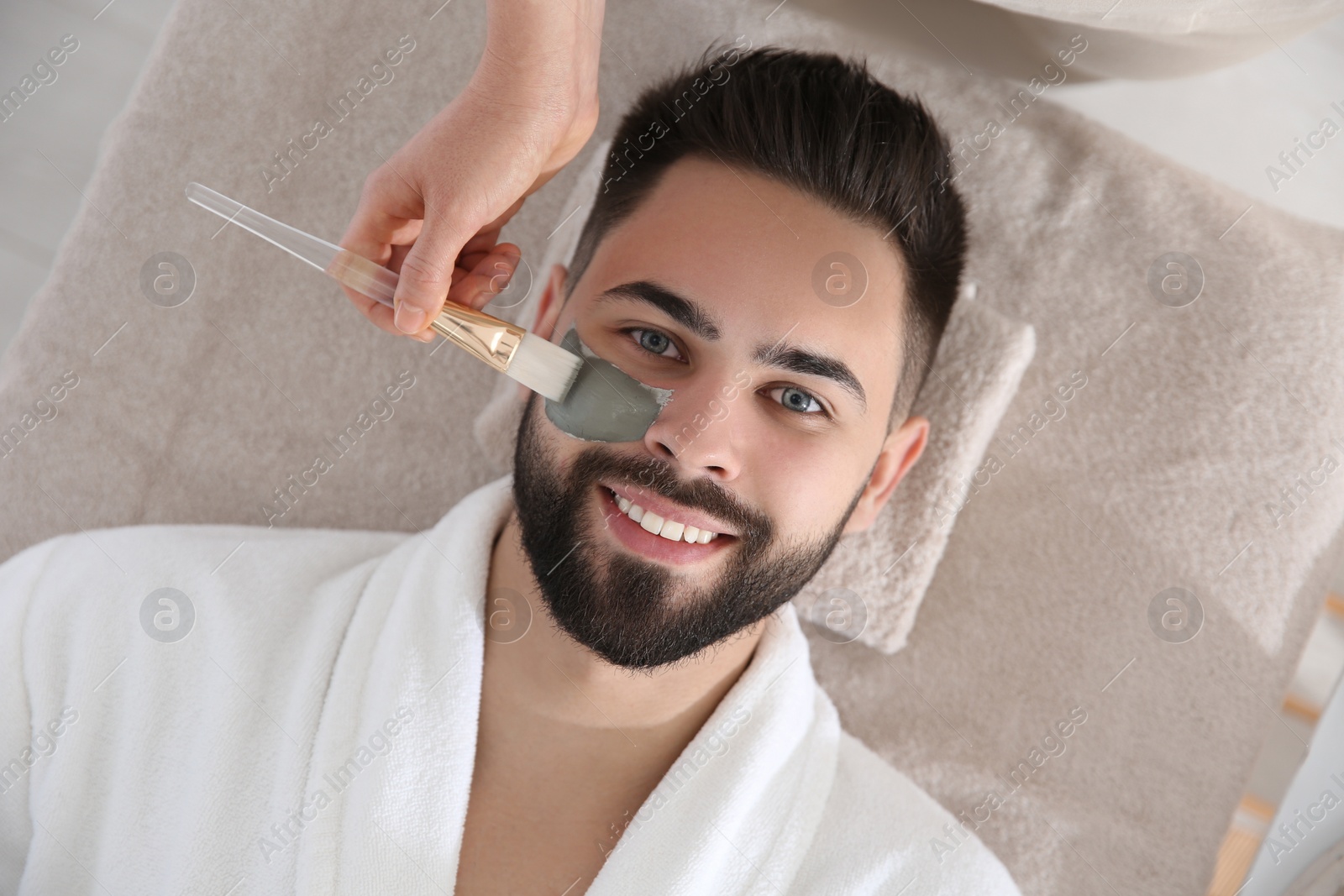 Photo of Cosmetologist applying mask on man's face in spa salon, top view