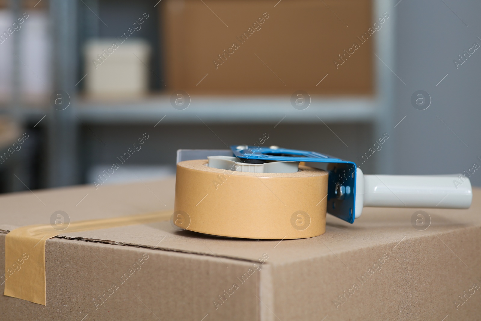 Photo of Adhesive tape dispenser on cardboard box indoors