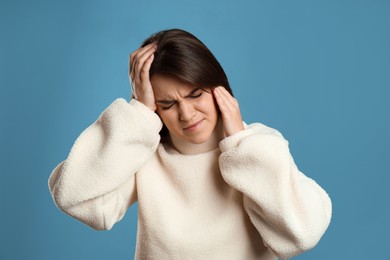 Photo of Young woman suffering from migraine on light blue background