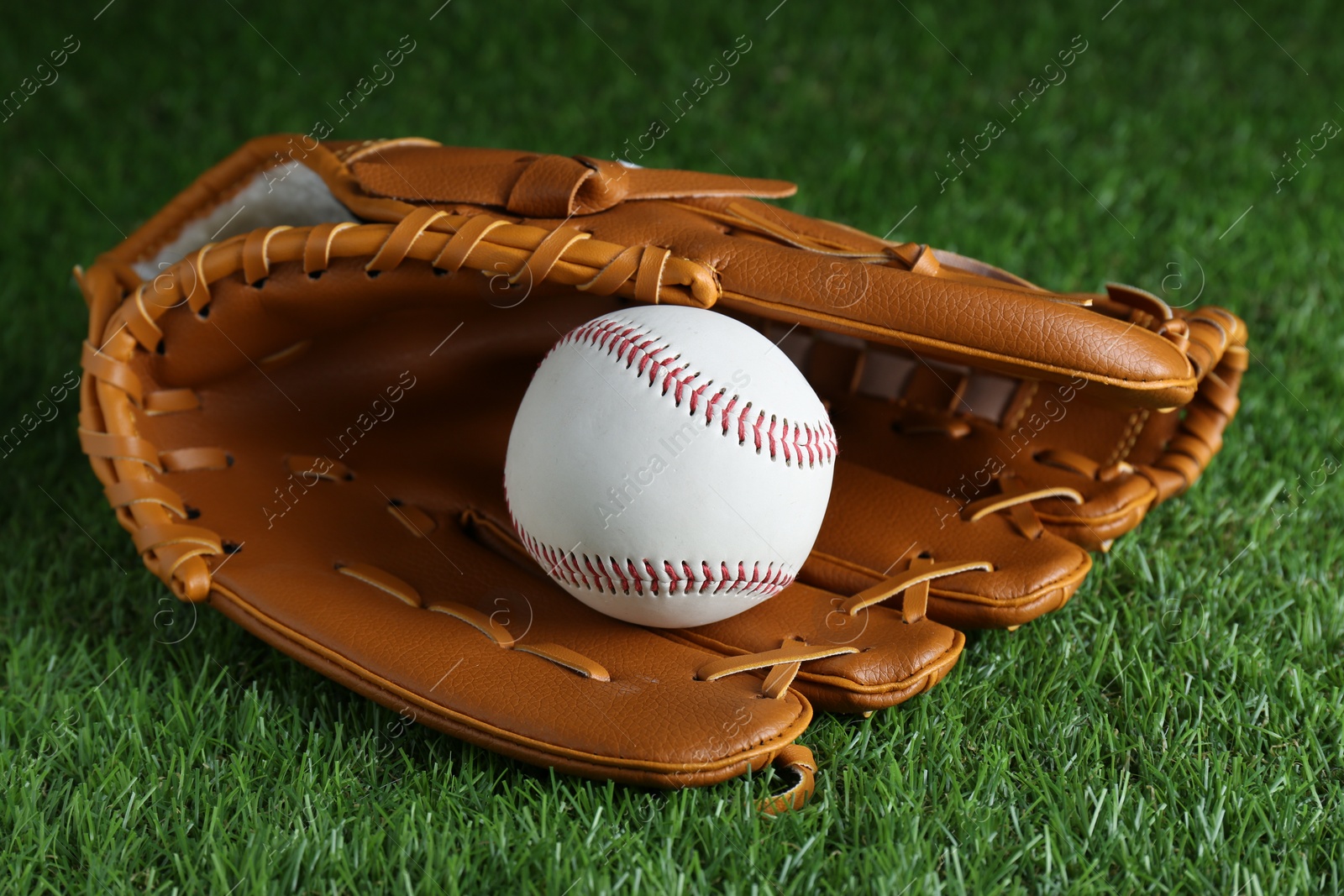 Photo of Catcher's mitt and baseball ball on green grass. Sports game