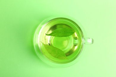 Photo of Cup of aromatic green tea with leaves on color background, top view