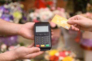 Woman using credit card for terminal payment in floral shop, closeup