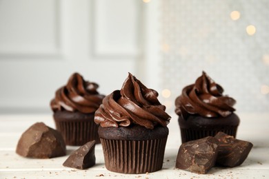 Photo of Delicious chocolate cupcakes with cream on white wooden table against blurred lights. Space for text