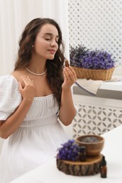 Photo of Beautiful young woman with bottle of essential oil at table indoors