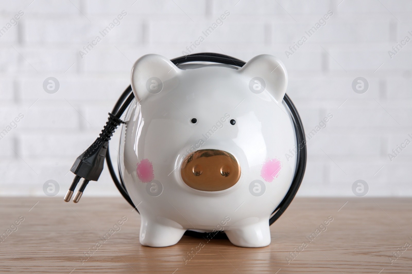 Photo of Piggy bank with power plug on wooden table. Energy saving concept