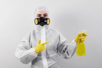 Woman in protective suit pointing at sprayer for cleaning mold near white wall