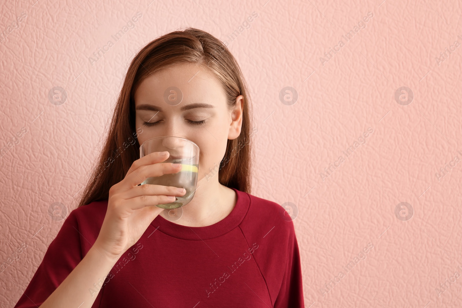 Photo of Young woman drinking lemon water on color background