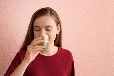 Young woman drinking lemon water on color background