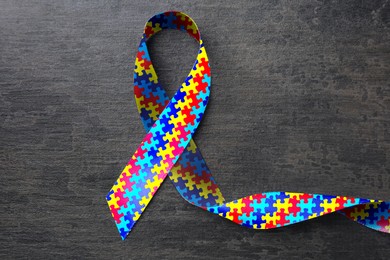 Image of World Autism Awareness Day. Colorful puzzle ribbon on grey stone background, top view