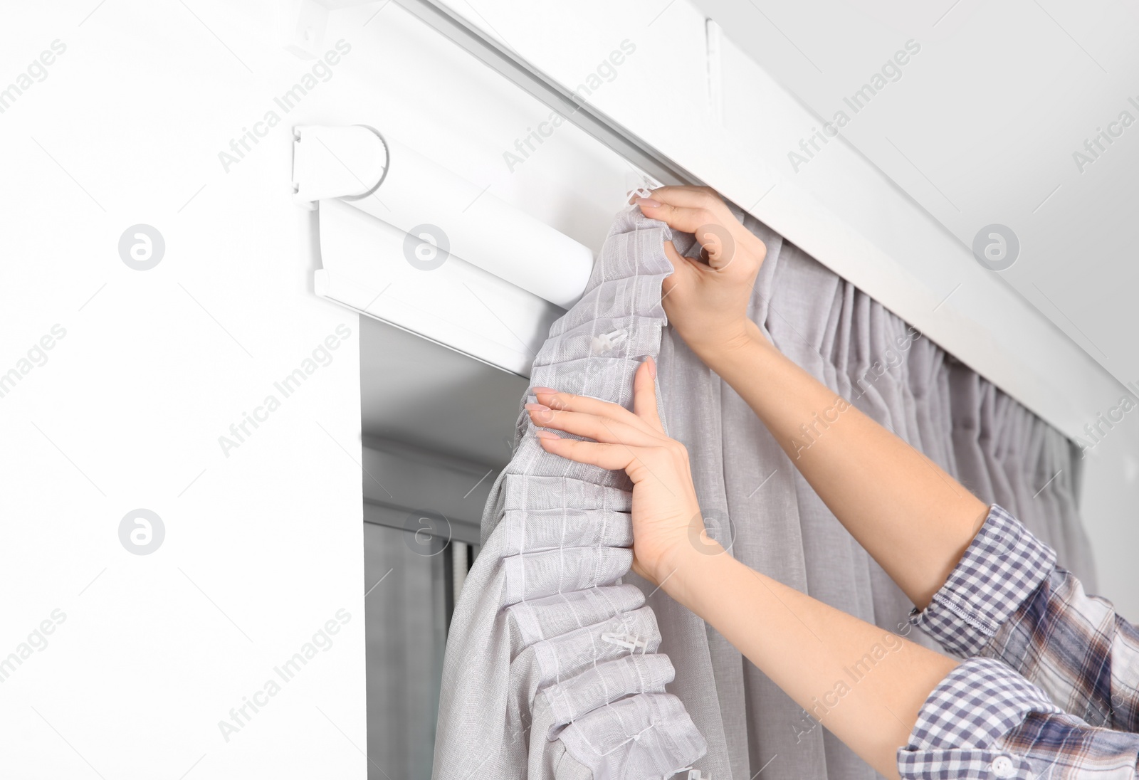 Photo of Woman hanging window curtain indoors, closeup. Interior decor element