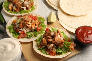 Photo of Delicious tacos with vegetables, meat and sauce on grey textured table