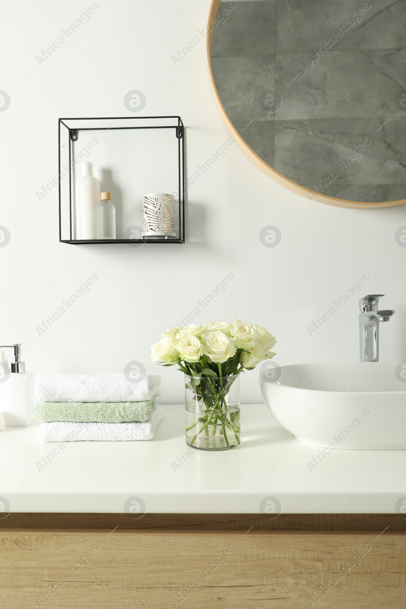 Photo of Bouquet of beautiful roses in vase and bath accessories near sink in bathroom