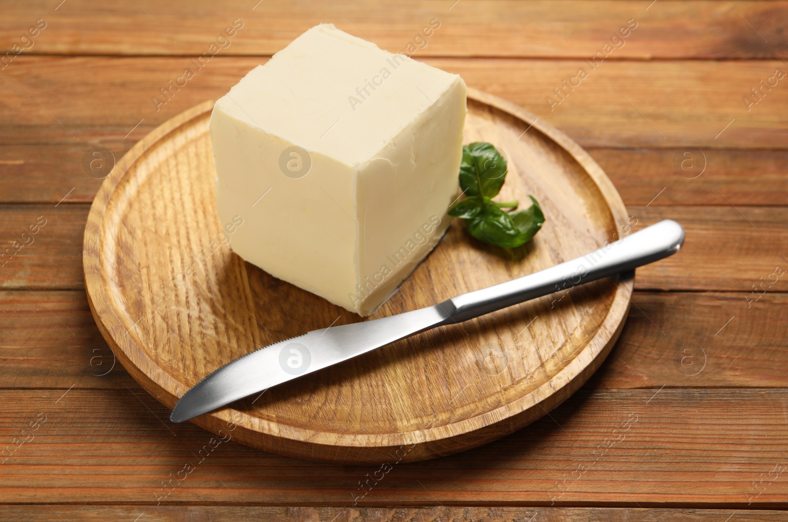 Photo of Block of tasty butter, knife and basil on wooden table