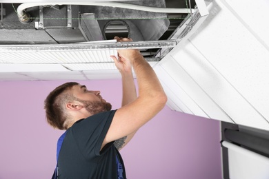 Young male technician checking air conditioner indoors