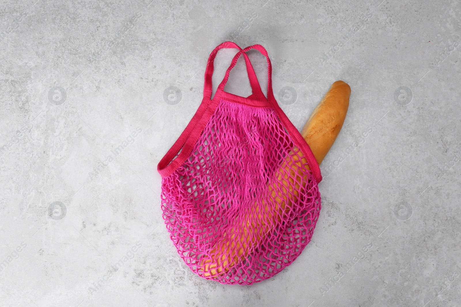 Photo of Pink net bag with baguette on light grey table, top view