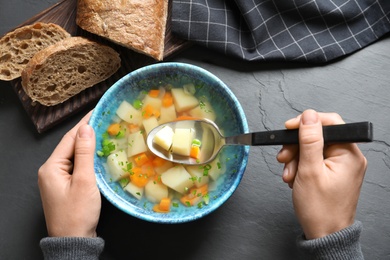 Photo of Woman eating fresh homemade vegetable soup at black table, top view