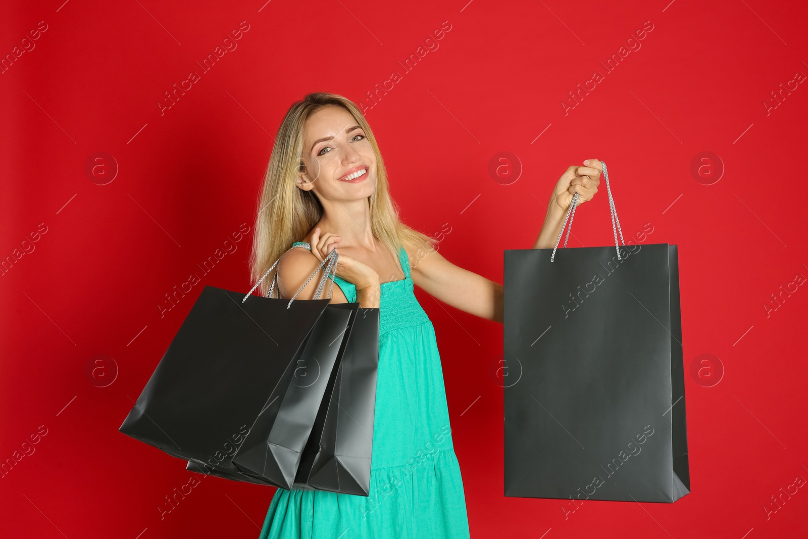 Photo of Happy young woman with shopping bags on red background. Black Friday Sale