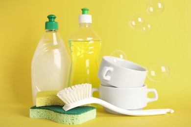 Cleaning supplies for dish washing and soap bubbles on yellow background