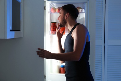 Photo of Man taking products out of refrigerator in kitchen at night