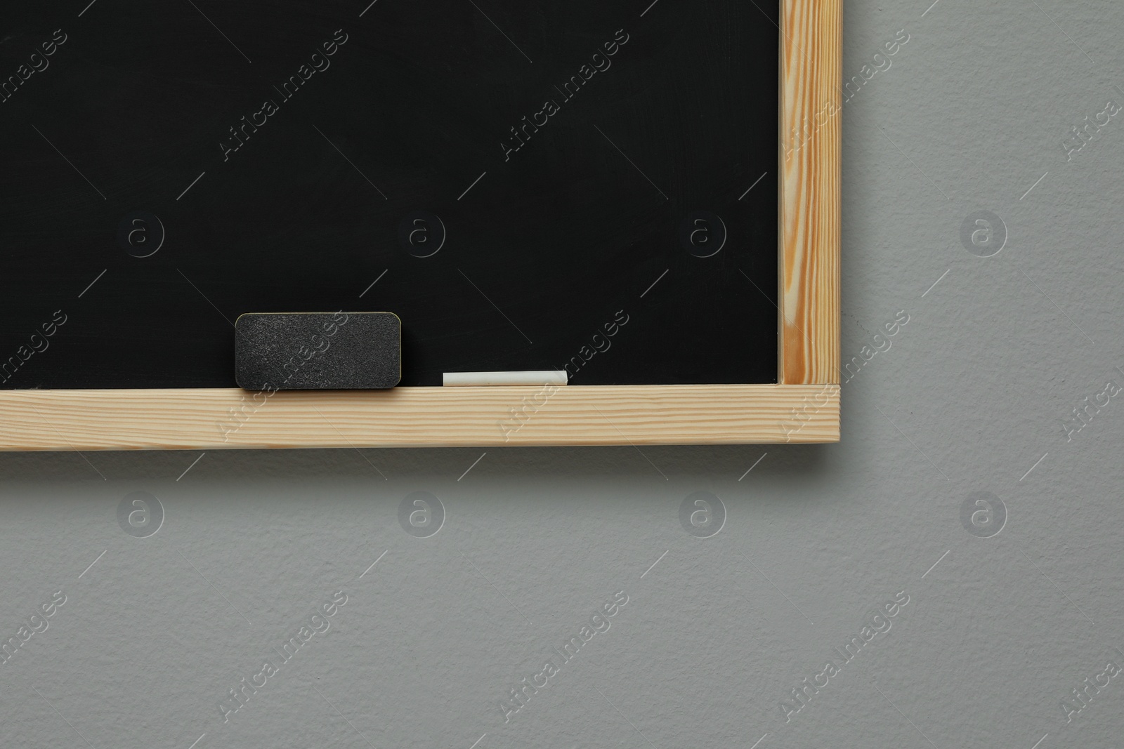 Photo of Clean blackboard with chalk and duster hanging on grey wall