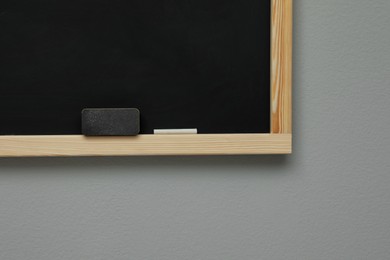 Photo of Clean blackboard with chalk and duster hanging on grey wall