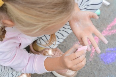 Little child drawing her hands with chalk outdoors, top view