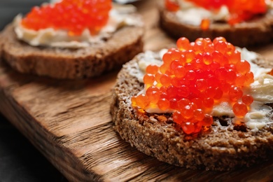 Photo of Delicious sandwich with red caviar on wooden board, closeup