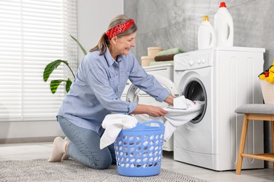 Happy housewife putting laundry into washing machine at home