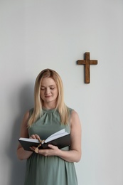 Young pregnant woman with Bible praying near light wall