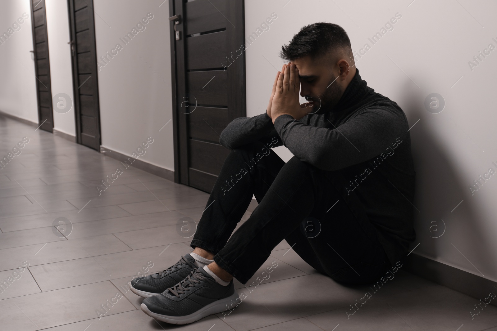 Photo of Sad man sitting on floor in hall. Space for text