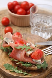 Photo of Tasty bruschetta with prosciutto, arugula, cheese and tomato on wooden board