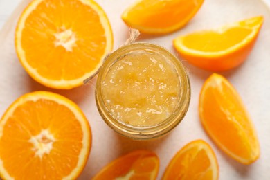 Photo of Jar of delicious orange jam and fresh fruits on plate, flat lay