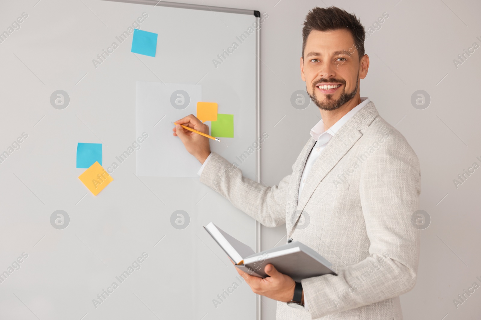 Photo of Happy teacher with book explaining something at whiteboard in classroom