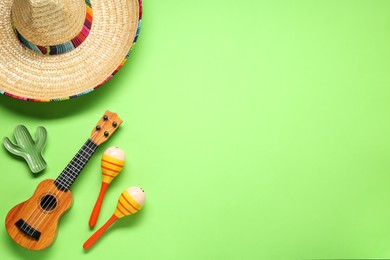 Photo of Mexican sombrero hat, maracas, toy cactus and guitar on green background, flat lay. Space for text