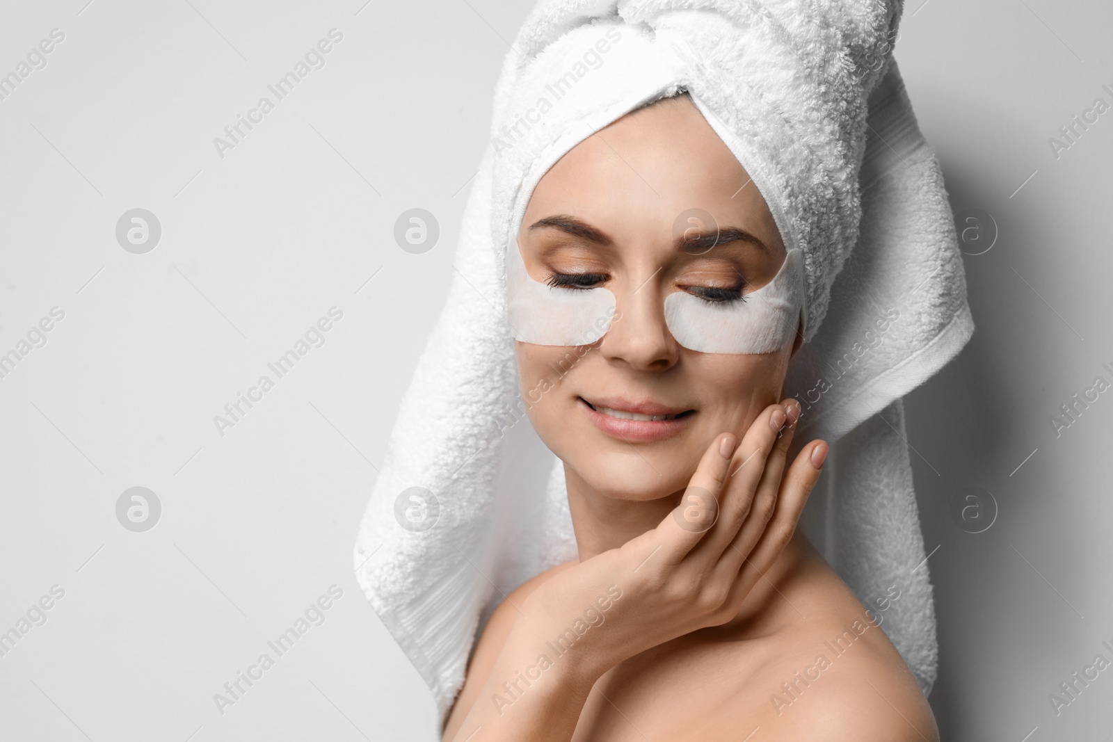 Photo of Beautiful woman with eye patches against light background, space for text. Facial mask