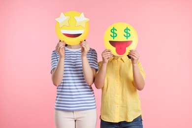 People covering faces with emoticons on pink background