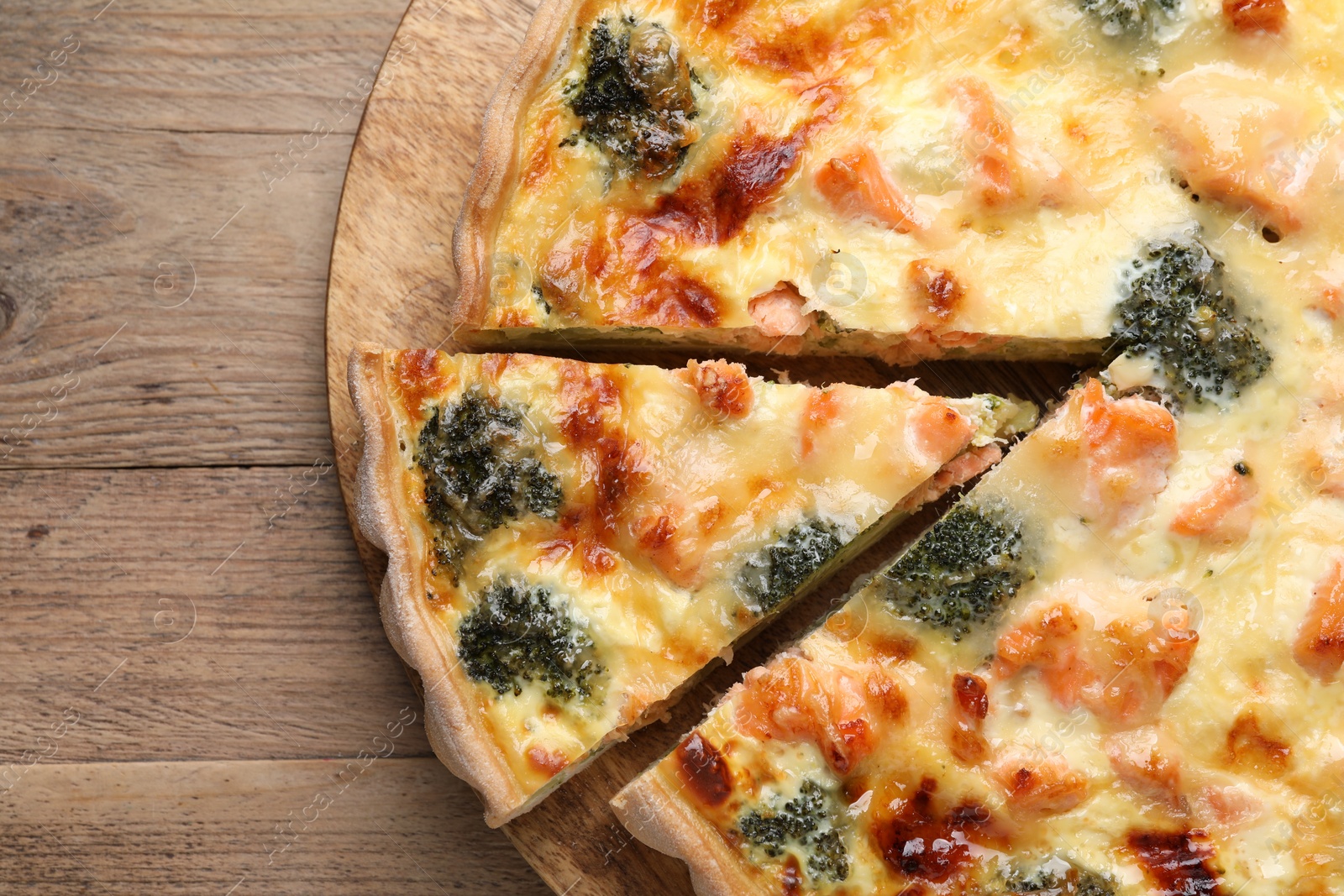 Photo of Delicious homemade quiche with salmon and broccoli on wooden table, top view