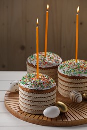 Photo of Traditional Easter cakes with sprinkles, candles and decorated eggs on white table