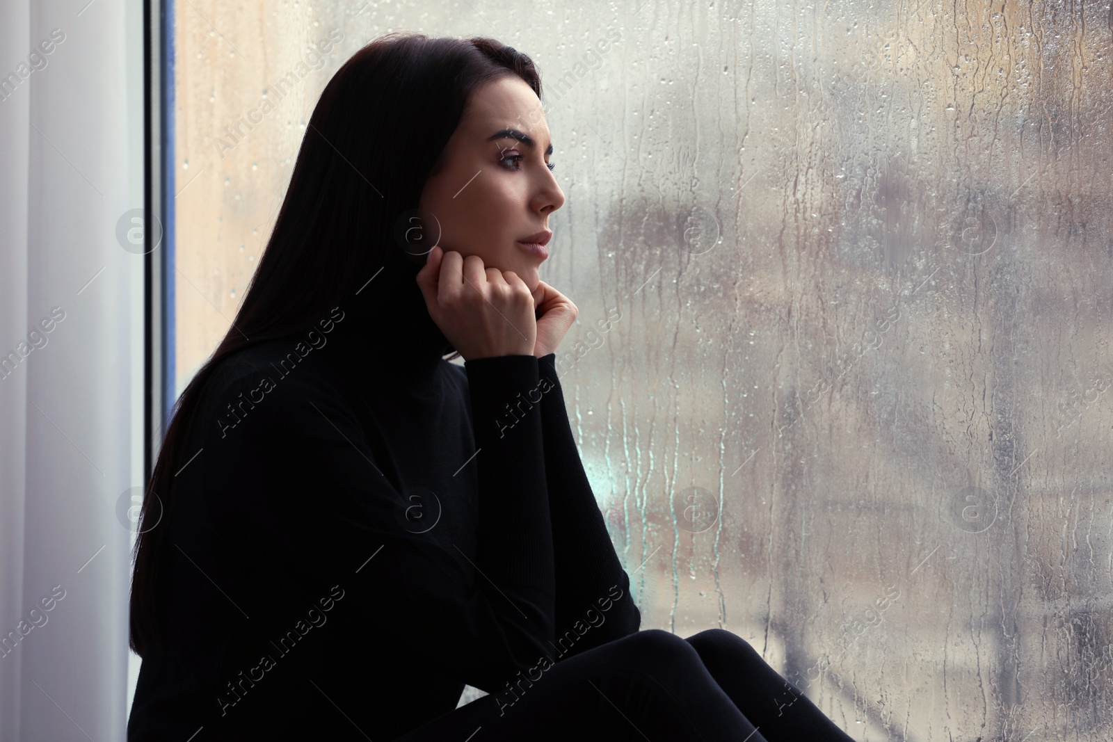 Photo of Depressed woman near window on rainy day, space for text