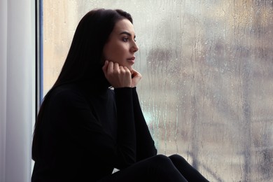 Depressed woman near window on rainy day, space for text