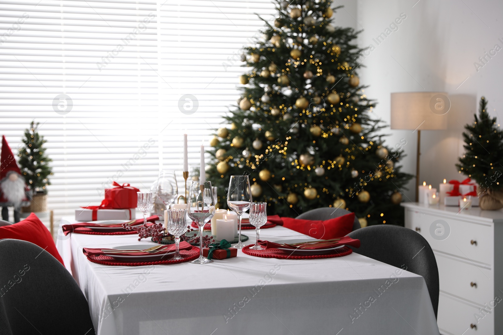 Photo of Christmas table setting with burning candles, gift box and dishware in room