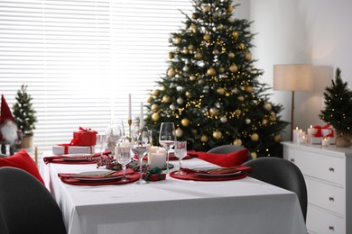 Photo of Christmas table setting with burning candles, gift box and dishware in room