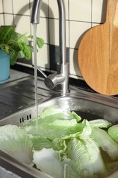 Photo of Pouring tap water on Chinese cabbage leaves in sink